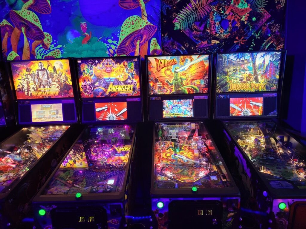 Four modern pinball machines glowing in a row under blacklight art