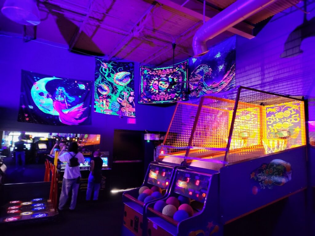 Skee-ball lanes and basketball hoops glowing under blacklight